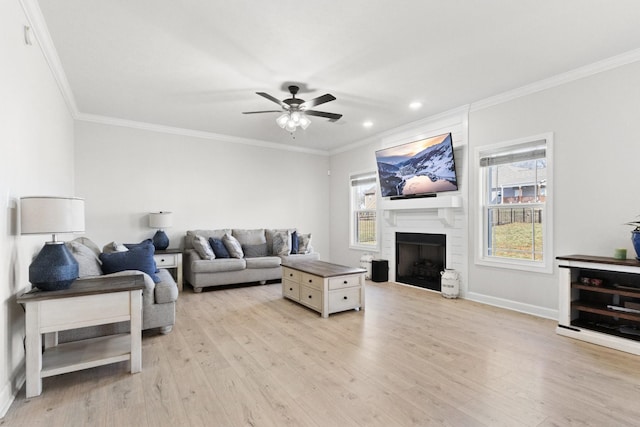 living area featuring a large fireplace, a ceiling fan, baseboards, ornamental molding, and light wood finished floors