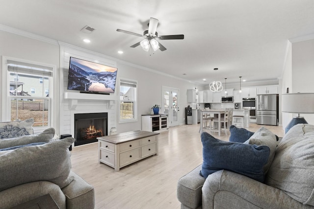 living room with light wood-type flooring, a fireplace, visible vents, and crown molding