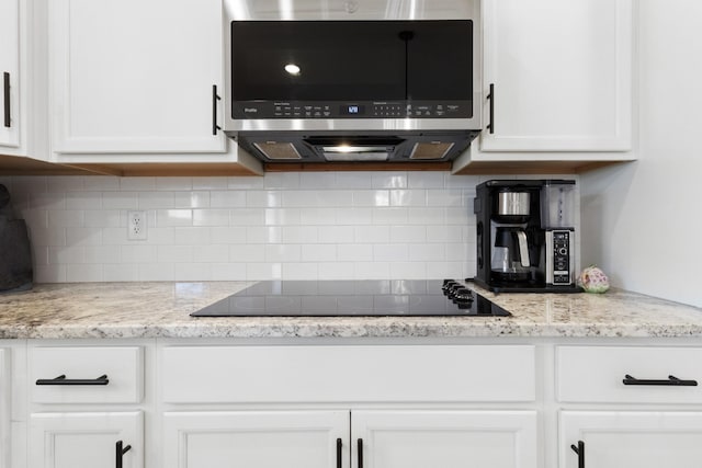 kitchen with light stone counters, stainless steel microwave, decorative backsplash, white cabinetry, and black electric cooktop