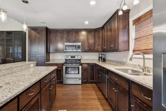 kitchen with hanging light fixtures, light stone countertops, appliances with stainless steel finishes, and a sink