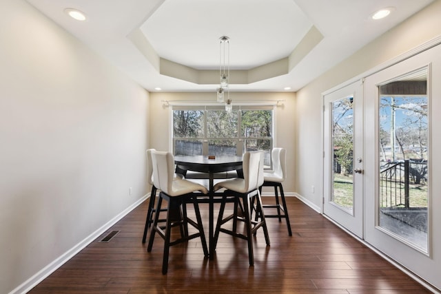 dining space with visible vents, a raised ceiling, dark wood finished floors, and french doors