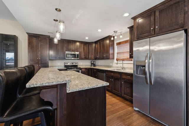 kitchen with decorative light fixtures, stainless steel appliances, a sink, dark brown cabinetry, and a kitchen island