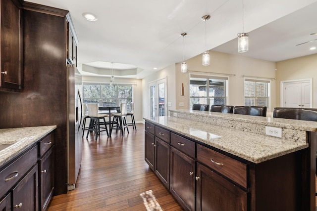 kitchen with dark brown cabinetry, dark wood finished floors, open floor plan, light stone countertops, and pendant lighting