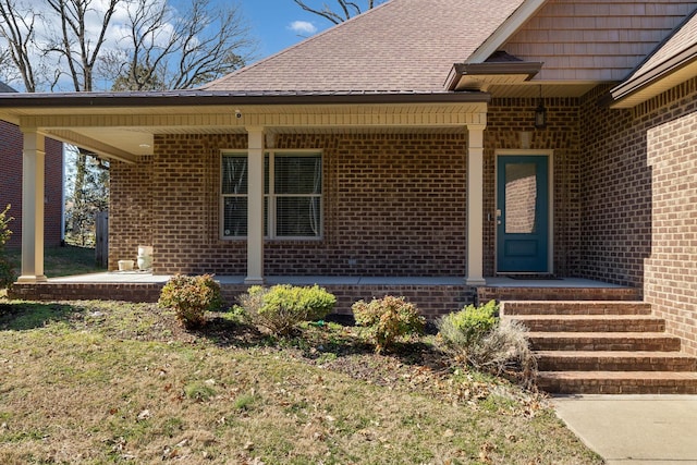 entrance to property with a patio area, brick siding, and roof with shingles