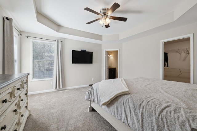 carpeted bedroom featuring ceiling fan, a tray ceiling, connected bathroom, and baseboards