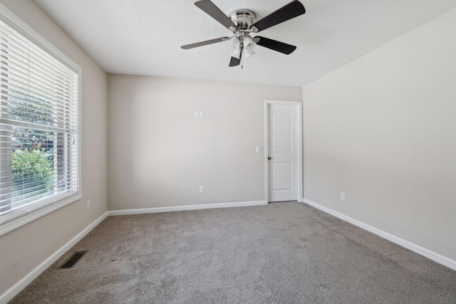 spare room featuring a textured ceiling, carpet floors, a ceiling fan, visible vents, and baseboards