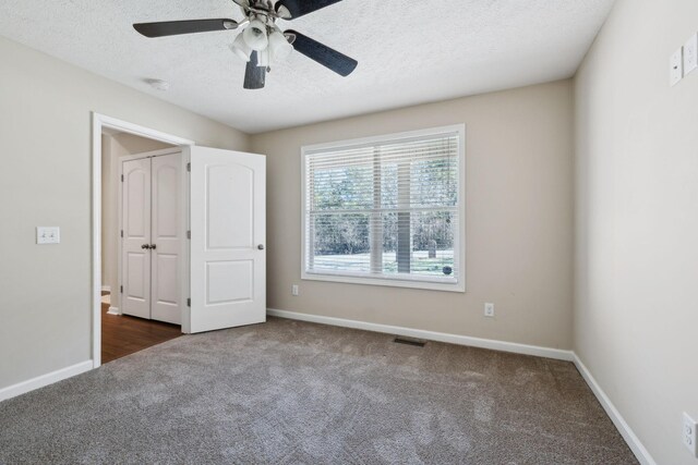 unfurnished bedroom featuring baseboards, visible vents, dark colored carpet, and a textured ceiling