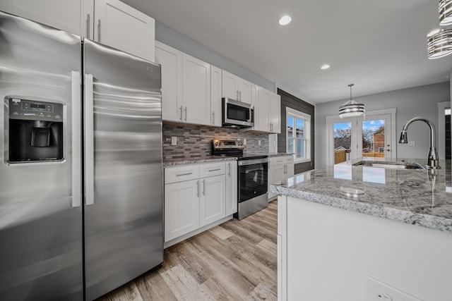 kitchen with white cabinetry, stainless steel appliances, a sink, and pendant lighting