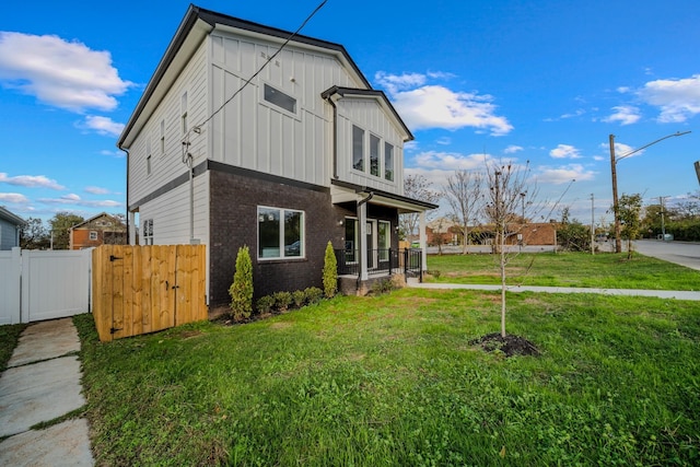 exterior space featuring brick siding, fence, a gate, board and batten siding, and a front yard