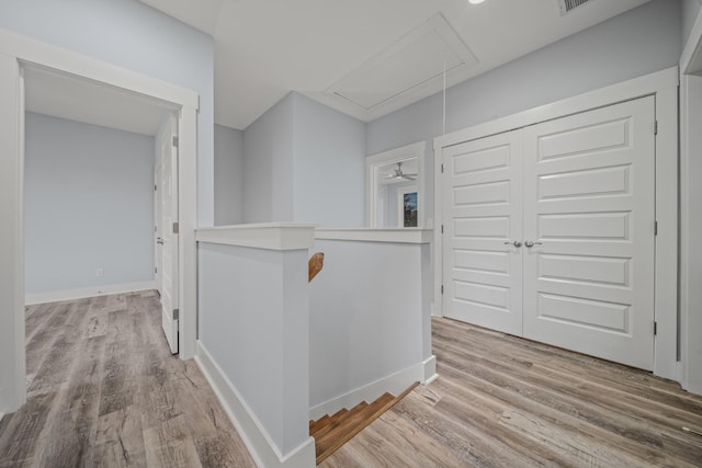 hallway with light wood-type flooring, attic access, baseboards, and an upstairs landing