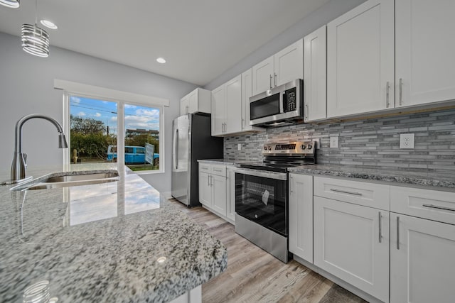 kitchen featuring white cabinets, light stone counters, stainless steel appliances, and a sink