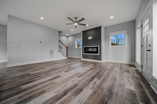 unfurnished living room with a large fireplace, stairway, wood finished floors, and visible vents