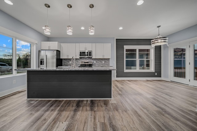 kitchen featuring stainless steel appliances, white cabinets, a center island with sink, and light stone counters