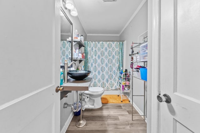 bathroom featuring crown molding, shower / bath combination with curtain, toilet, a sink, and wood finished floors