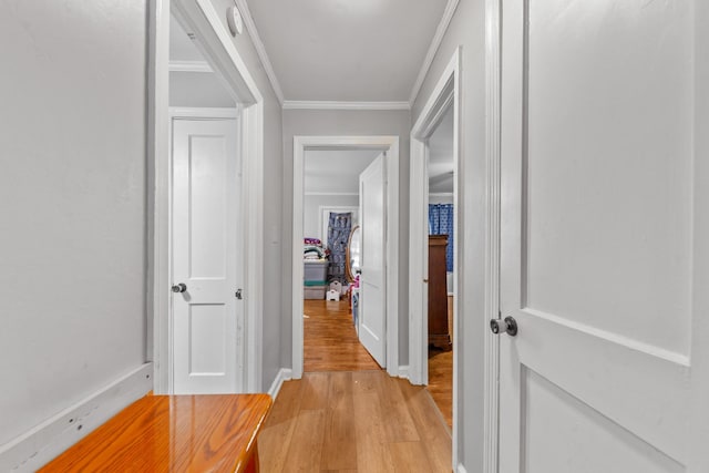 corridor featuring light wood-style floors, baseboards, and crown molding