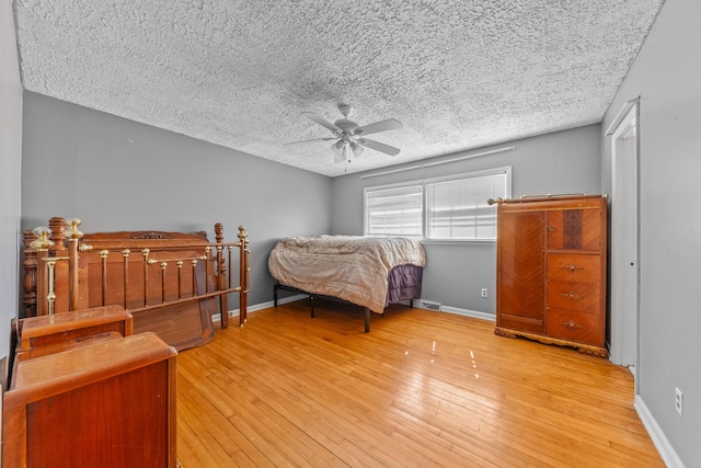 bedroom featuring visible vents, baseboards, a ceiling fan, light wood-style flooring, and a textured ceiling