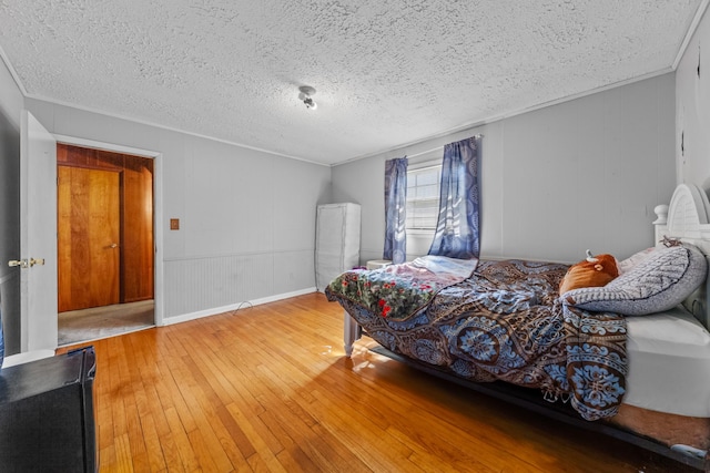 bedroom with a textured ceiling, ornamental molding, and wood finished floors