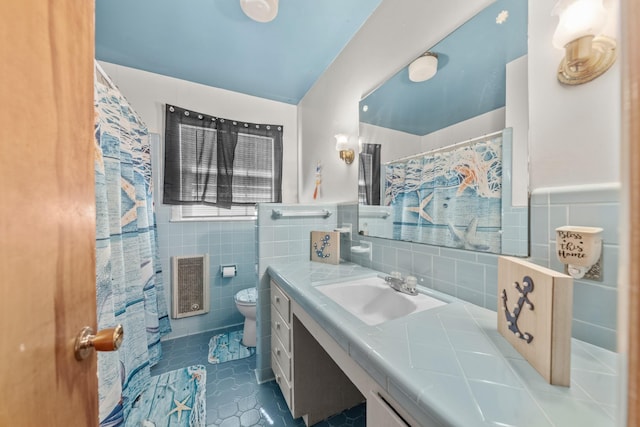 bathroom featuring tile patterned flooring, toilet, vanity, tile walls, and wainscoting