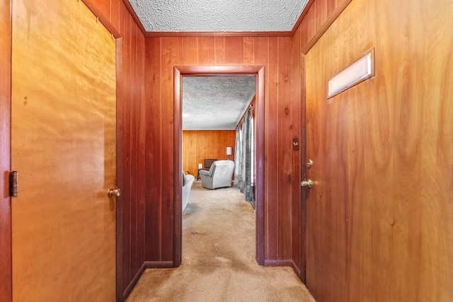 hallway with light carpet, wooden walls, and a textured ceiling