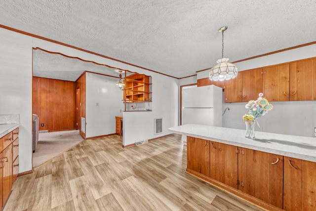 kitchen with brown cabinetry, freestanding refrigerator, light countertops, light wood-style floors, and pendant lighting