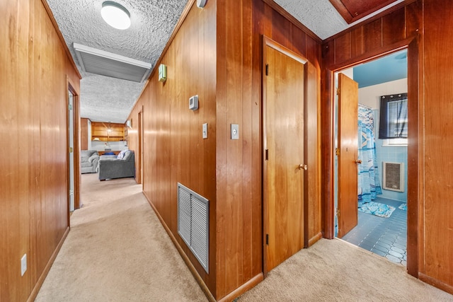 hallway with light colored carpet, visible vents, wood walls, and a textured ceiling