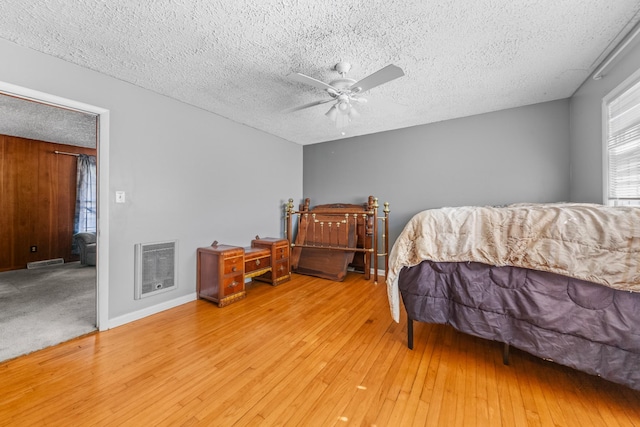 bedroom featuring a textured ceiling, ceiling fan, wood finished floors, visible vents, and heating unit