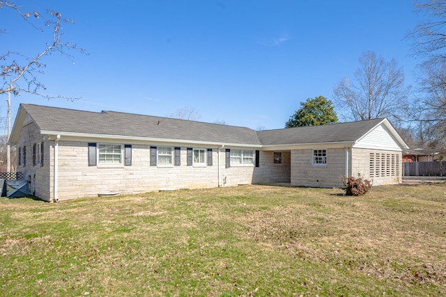 back of property with a shingled roof, stone siding, and a lawn