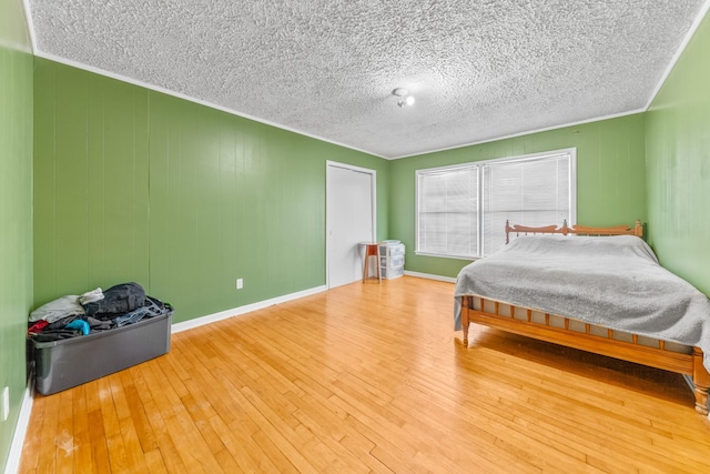 bedroom featuring baseboards, a textured ceiling, ornamental molding, and wood finished floors