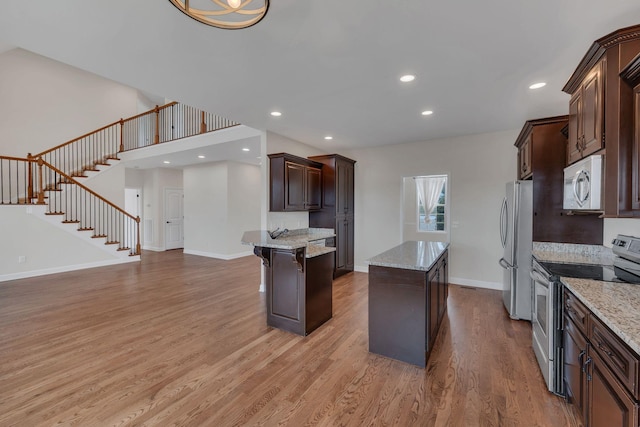 kitchen featuring light stone counters, light wood-style flooring, dark brown cabinetry, stainless steel appliances, and a kitchen island