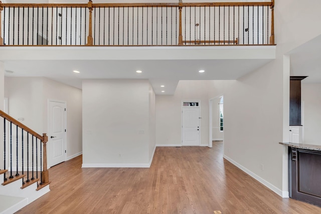 unfurnished living room with baseboards, recessed lighting, stairs, and light wood-style floors