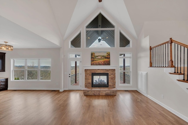 unfurnished living room featuring high vaulted ceiling, a wealth of natural light, a fireplace, and wood finished floors