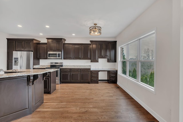 kitchen with stainless steel appliances, light stone counters, light wood-style flooring, and dark brown cabinetry