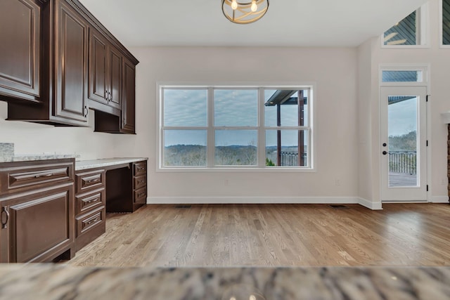 kitchen with light wood-style flooring, baseboards, built in desk, and dark brown cabinets