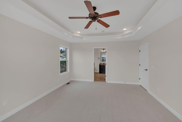 spare room featuring recessed lighting, a raised ceiling, light colored carpet, and baseboards