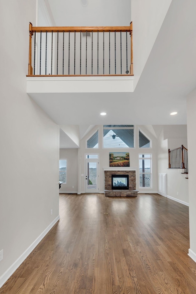 unfurnished living room featuring a fireplace, a towering ceiling, baseboards, and wood finished floors