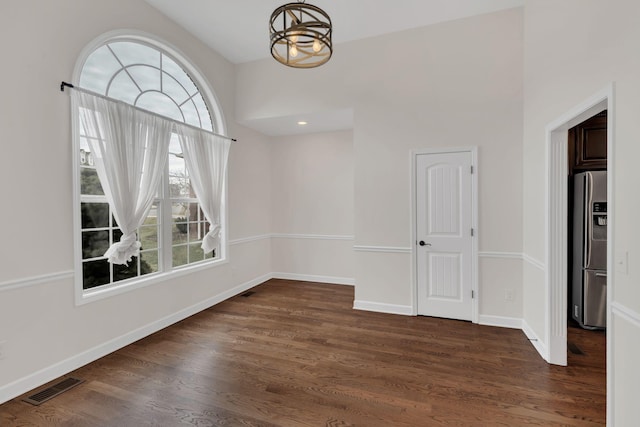 unfurnished dining area with dark wood-style floors, baseboards, visible vents, and a chandelier