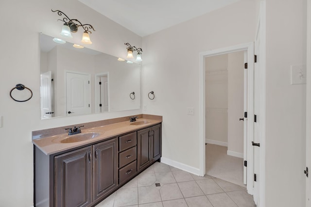 full bath with a walk in closet, double vanity, a sink, baseboards, and tile patterned floors