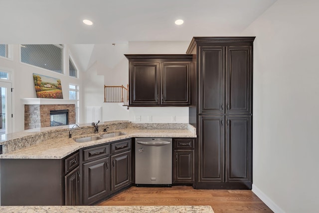 kitchen with light wood finished floors, a sink, a stone fireplace, dark brown cabinets, and dishwasher