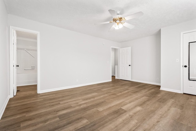 unfurnished bedroom with a ceiling fan, a textured ceiling, ensuite bath, wood finished floors, and baseboards