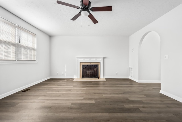 unfurnished living room featuring arched walkways, dark wood-type flooring, a fireplace with flush hearth, and visible vents