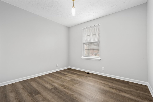 unfurnished room with visible vents, dark wood finished floors, a textured ceiling, and baseboards