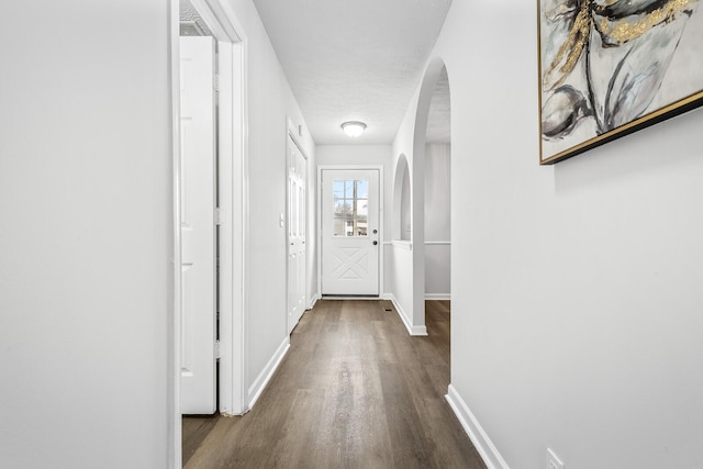 corridor with arched walkways, dark wood-type flooring, and baseboards