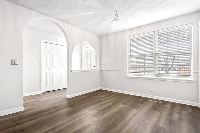 empty room featuring a textured ceiling, dark wood-type flooring, visible vents, and baseboards