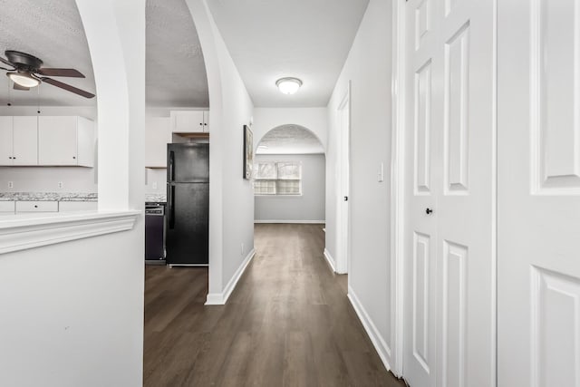 hall with dark wood-type flooring, arched walkways, a textured ceiling, and baseboards