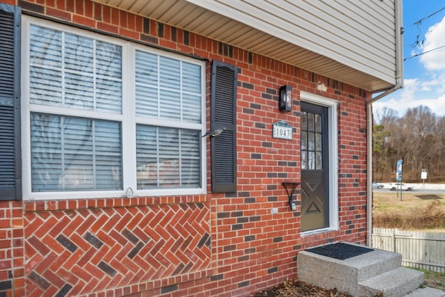 view of exterior entry with brick siding and fence