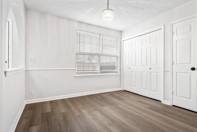 unfurnished bedroom with a closet, a textured ceiling, baseboards, and wood finished floors