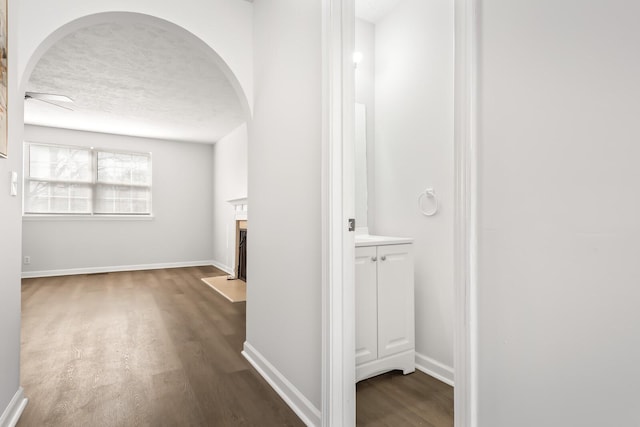 hallway with baseboards, arched walkways, dark wood finished floors, and a textured ceiling