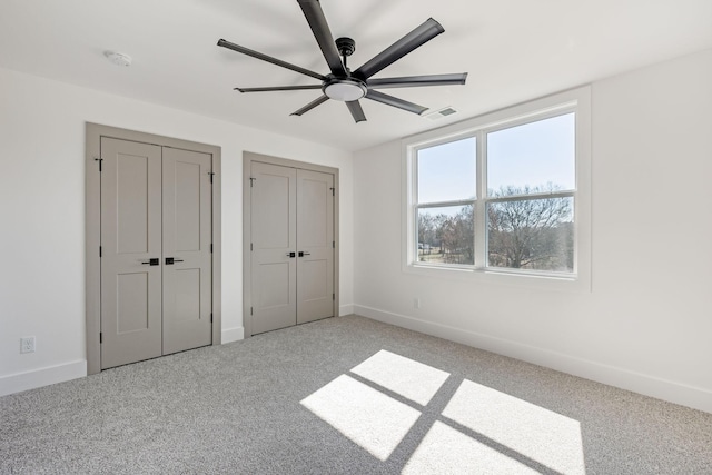 unfurnished bedroom featuring two closets, light colored carpet, visible vents, a ceiling fan, and baseboards