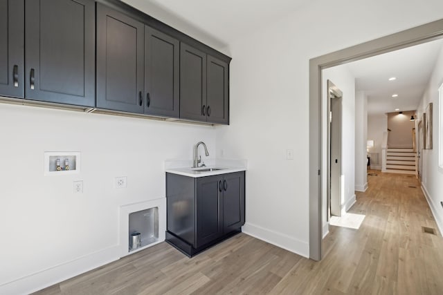 washroom with washer hookup, a sink, baseboards, cabinet space, and light wood finished floors