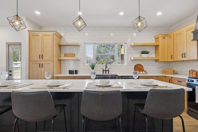 kitchen featuring stainless steel range oven, backsplash, a sink, and light brown cabinetry